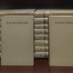 Puede incluir: Un conjunto de 18 libros de Fiódor Dostoievski, encuadernados en beige con letras doradas. Los libros están dispuestos en dos pilas, con los lomos hacia afuera. Los libros están numerados del 1 al 18.