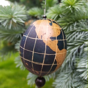 May include: A globe-shaped Christmas ornament with a black and gold design. The ornament is hanging from a tree branch.