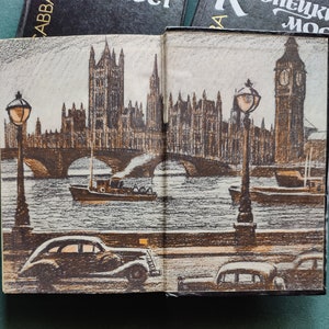 May include: An open book with a drawing of a bridge over a river with buildings in the background. The buildings are brown and gray and have many windows. There are two streetlights on either side of the bridge. The river is a light blue color. The book is open to a page with the words 'London Bridge' on the top of the page.
