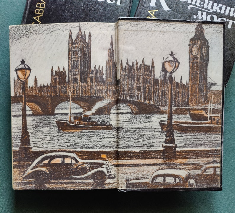 May include: An open book with a drawing of a bridge over a river with buildings in the background. The buildings are brown and gray and have many windows. There are two streetlights on either side of the bridge. The river is a light blue color. The book is open to a page with the words 'London Bridge' on the top of the page.