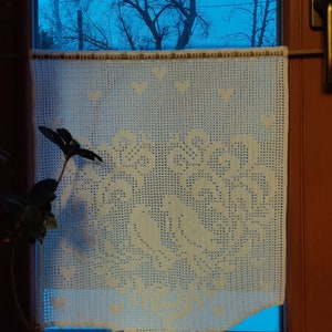 以下が含まれることがあります： 白いレースのカーテンで、裾は波打っていて、花柄のデザインが施されています。カーテンは窓にかけられていて、青い空と木々が見えます。