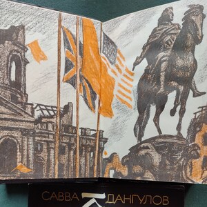 May include: An open book with a pencil drawing of a city scene with a statue of a person on horseback. The city scene includes buildings, flags, and a sky. The book is open to a page with the text 'Савва Дангулов' at the bottom of the page.