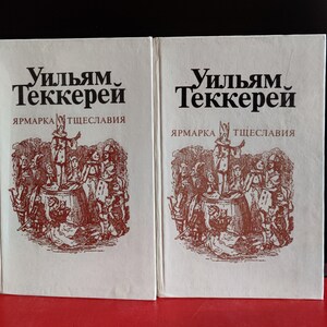 May include: Two white book covers with the title "William Makepeace Thackeray" and the text "Vanity Fair" in black lettering. The covers feature a red illustration of a group of people gathered around a barrel.