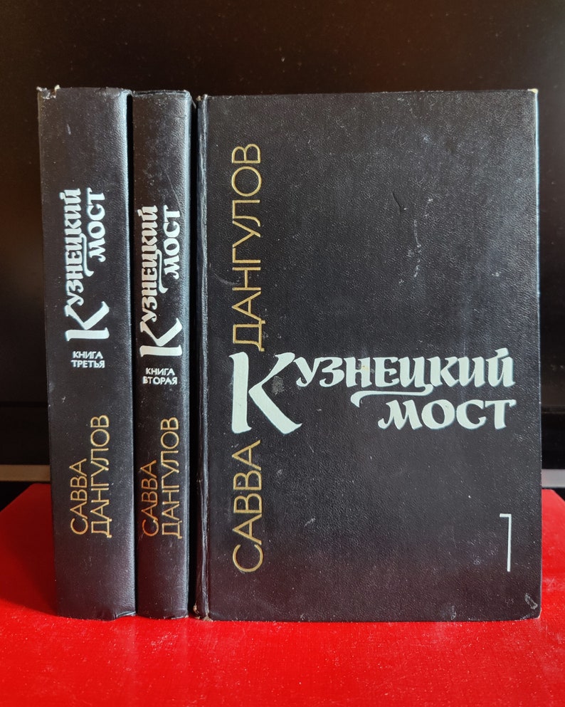 May include: Three black hardcover books with gold lettering. The books are titled 'Kuznetskiy Most' and 'Savva Dangulov.' The first book is labeled 'Kniga Tretya' (Book Three), the second book is labeled 'Kniga Vtoraya' (Book Two), and the third book is labeled '1'.