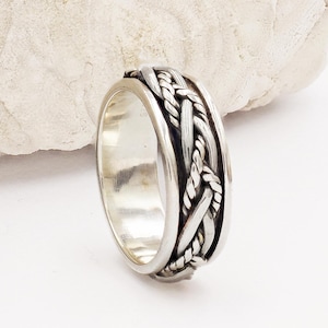 May include: A silver ring with a braided design. The band is wide and the braid is intricate.