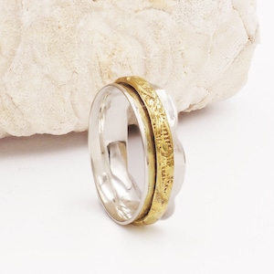 May include: A silver and gold spinning ring with a decorative pattern. The ring is on a white background.