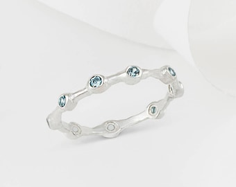 May include: A silver band ring with a textured design and small blue gemstones set into the band.