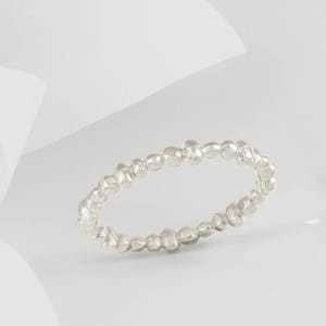 May include: A silver ring with a textured, beaded design. The ring is made of small, irregular beads that are connected together to form a continuous band.