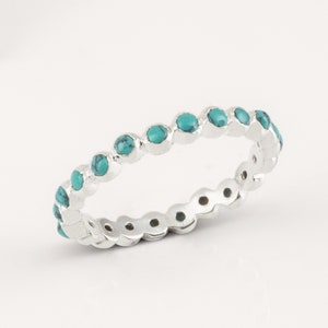 Op de afbeelding: Een zilveren ring met een rij turquoise stenen rond de band.