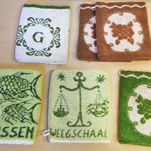 May include: Five green and white embroidered hand towels with different designs. The towels feature a letter G, a fish, a scale, and two floral designs.