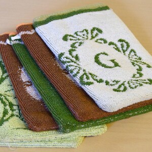 May include: A stack of five green, brown, and white hand towels with embroidered green floral designs and the letter "G" on the top towel.