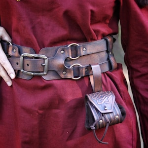 Leather coin pouch worn on a belt alongside other fantasy leather accessories. Small embossed pouch with geometric Celtic patterns, handcrafted from vegetable-tanned leather and finished with artisanal aging. Designed to carry coins, dice, or small valuables. Suitable for Viking, Celtic, dwarven, or medieval-inspired outfits, LARP, cosplay, Renaissance fairs, or fantasy-themed everyday wear.