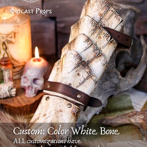 Bone-white custom version of the Dragon Scale Bracer presented on a medieval-style altar with candles and skulls. A unique accessory for necromancer LARP characters, undead warriors, or pale elven cosplays. Crafted in vegetable-tanned leather and detailed with a bone-effect finish. Fully handmade and customizable, this vambrace brings eerie presence to your fantasy gear.