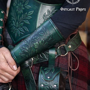 Floral embossed leather bracer and matching green leather coin pouch worn with a renaissance style belt, ideal for elves, witches, herbalists and nobles at LARP or Renaissance Faire events. The vegetable tanned leather shows detailed leaf and wildflower patterns, paired with a soft suede pouch for coins or small items. The image highlights the elegant elven aesthetic and how the pouch hangs securely from the belt loop.