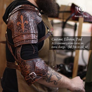 May include: A brown leather elbow pad with detailed embossed floral and fleur-de-lis patterns. The armour has multiple articulated plates and is fastened with buckles and straps. The text "Custom: Elbow Pad" is visible.