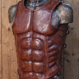 Front view of a Roman leather musculata cuirass, handcrafted with brown aged leather and metallic rivets. The armor features sculpted abdominal muscles and distressed textures for a realistic battle-worn look. Ideal for Roman gladiator cosplay, LARP armor, or historical reenactment costume. Made from eco-tanned full-grain leather with epic weathering techniques.