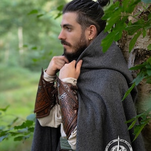 Side profile of a fantasy ranger in a grey cloak, wearing brown Gondorian vambraces with White Tree embossing. Inspired by LOTR and Aragorn’s gear, these bracers are crafted for LARP, cosplay, and Tolkien fans. Elven feather engravings add authenticity. Ideal for medieval reenactments, roleplay, and portraying Gondor’s defenders or Citadel rangers. Premium handcrafted leather accessory. White tree leather bracers fantasy ranger armor LARP bracers medieval cosplay accessory elven warrior costume