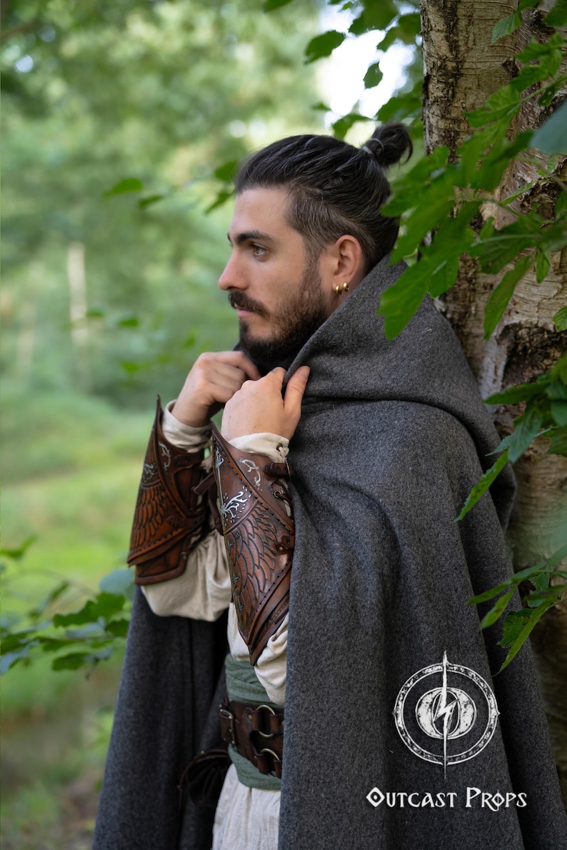 Side profile of a fantasy ranger in a grey cloak, wearing brown Gondorian vambraces with White Tree embossing. Inspired by LOTR and Aragorn’s gear, these bracers are crafted for LARP, cosplay, and Tolkien fans. Elven feather engravings add authenticity. Ideal for medieval reenactments, roleplay, and portraying Gondor’s defenders or Citadel rangers. Premium handcrafted leather accessory. White tree leather bracers fantasy ranger armor LARP bracers medieval cosplay accessory elven warrior costume