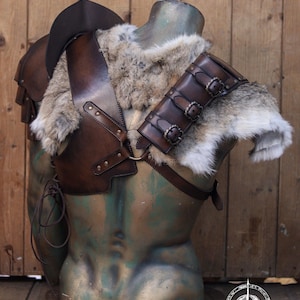 Side view of the barbarian leather armor showing the shoulder section padded with thick grey rabbit fur. A series of dark brown leather straps with aged buckles secure the fur onto the shoulder harness. Perfect for Viking cosplay, medieval warriors or LARP costumes. The fur piece adds wild realism and can be detached for modular costume customization. Artisan-crafted from full grain leather.