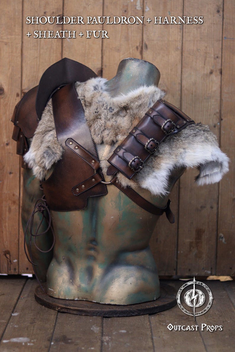 Side view of the barbarian leather armor showing the shoulder section padded with thick grey rabbit fur. A series of dark brown leather straps with aged buckles secure the fur onto the shoulder harness. Perfect for Viking cosplay, medieval warriors or LARP costumes. The fur piece adds wild realism and can be detached for modular costume customization. Artisan-crafted from full grain leather.