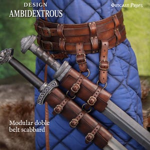 Puede incluir: Un sistema de funda de doble cinturón modular de cuero marrón con hebillas de metal, que sostiene dos espadas. El equipo se lleva sobre una túnica azul acolchada. El texto dice: DESIGN AMBIDEXTROUS, OUTCAST PROPS y Modular doble belt scabbard.