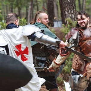 Live-action LARP battle photo featuring a warrior wearing the brown Roman leather musculata while clashing swords with a templar. The armor is paired with fur and tattered gear, ideal for barbarian or gladiator cosplay. This immersive shot highlights the armor in motion, showcasing its comfort, durability, and visual impact during roleplay combat scenes.