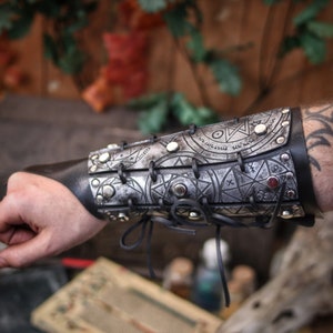 Silver leather bracer for LARP and fantasy cosplay, engraved with alchemical symbols and mystical geometry. Decorated with metal studs and polished beads for a gothic warlock or dark wizard look. Handmade from vegetable-tanned Spanish leather, adjustable and resistant. Perfect for witches, ritualists, or demon hunters in immersive fantasy roleplay.