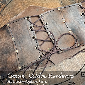 Back view of aged brown leather corset featuring custom golden brass rivets and eyelets, hand-laced with leather cords for adjustable fit. Designed for witches, alchemists, and steampunk adventurers, this custom LARP corset option adds warmth and elegance to renaissance fair clothing or fantasy outfits. Each piece is handmade from full-grain vegetable-tanned leather using eco-friendly dyes and aging techniques.