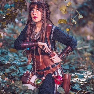 Female adventurer in the forest wearing the old brown leather corset model. The new edition is crafted in aged brown with nickel hardware and more elegant buckles. Designed for witches, alchemists, and fantasy LARP characters, this steampunk waist cincher combines historical style and eco-tanned leather craftsmanship, ideal for renaissance fairs, gothic events, and fantasy festivals.