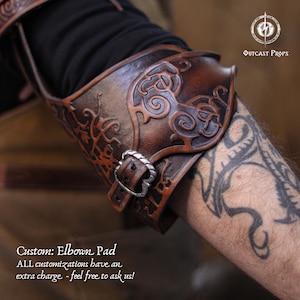 May include: A brown leather elbow pad featuring detailed embossed patterns and a silver buckle. The image includes text indicating it's a custom design. The Outcast Props logo is visible. The pad is designed for protection.