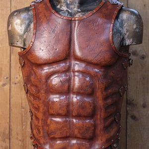 Front view of a Roman leather musculata cuirass, handcrafted with brown aged leather and metallic rivets. The armor features sculpted abdominal muscles and distressed textures for a realistic battle-worn look. Ideal for Roman gladiator cosplay, LARP armor, or historical reenactment costume. Made from eco-tanned full-grain leather with epic weathering techniques.