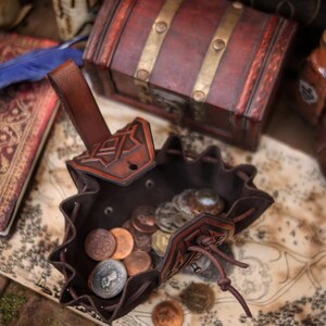 Top view of an open leather coin pouch filled with metal coins on a fantasy map. Handcrafted from vegetable tanned leather with embossed geometric details and a soft suede interior. Compact medieval belt pouch for coins, dice, keys, small jewelry, or tobacco. Ideal for Viking, Celtic, dwarf, fantasy styles, LARP, Renaissance fairs, cosplay, and everyday carry.