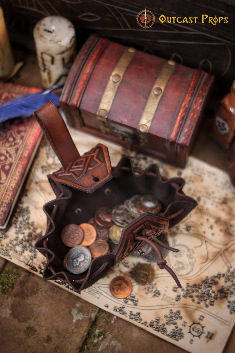 Top view of an open leather coin pouch filled with metal coins on a fantasy map. Handcrafted from vegetable tanned leather with embossed geometric details and a soft suede interior. Compact medieval belt pouch for coins, dice, keys, small jewelry, or tobacco. Ideal for Viking, Celtic, dwarf, fantasy styles, LARP, Renaissance fairs, cosplay, and everyday carry.