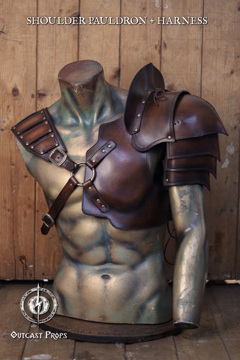 Mannequin bust wearing full barbarian leather shoulder armor set with crossed harness and riveted pauldrons. The armor is aged brown, handcrafted in vegetable-tanned leather with visible patina and hand-stitched details. Worn over a dark medieval shirt, this larp armor set includes sword scabbard on the back. Perfect for viking costume, post-apocalyptic larp, or warrior cosplay outfit.