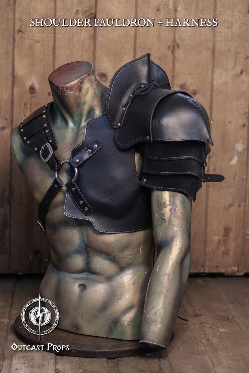 Pu&ograve; includere: Set di spallacci e imbracatura in pelle nera esposto su un manichino senza testa. L'armatura presenta una protezione per le spalle a strati, cinghie e fibbie metalliche. Il testo "SHOULDER PAULDRON + HARNESS" &egrave; in alto.