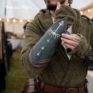 Fantasy LARP costume detail showing green Gondor vambrace engraved with White Tree, worn by an elven ranger. Embossed leather inspired by Aragorn and LOTR aesthetics. Adjustable and handmade, this bracer suits cosplay, Tolkien events, and medieval warriors. Ideal for portraying Gondorian soldiers or Middle-earth scouts. Evokes characters like Boromir, Faramir, and Númenórean descendants.