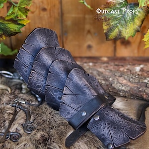 Black dragon scale leather bracer displayed on a fur and wooden background with medieval props. This handcrafted piece is ideal for LARP warriors, Viking cosplay, and medieval reenactment. Made from vegetable-tanned leather and detailed with Outcast Props’ unique weathering and aging finish, the scales evoke power and mystery—perfect for orc armor, dark ranger costumes, or monster hunter kits.