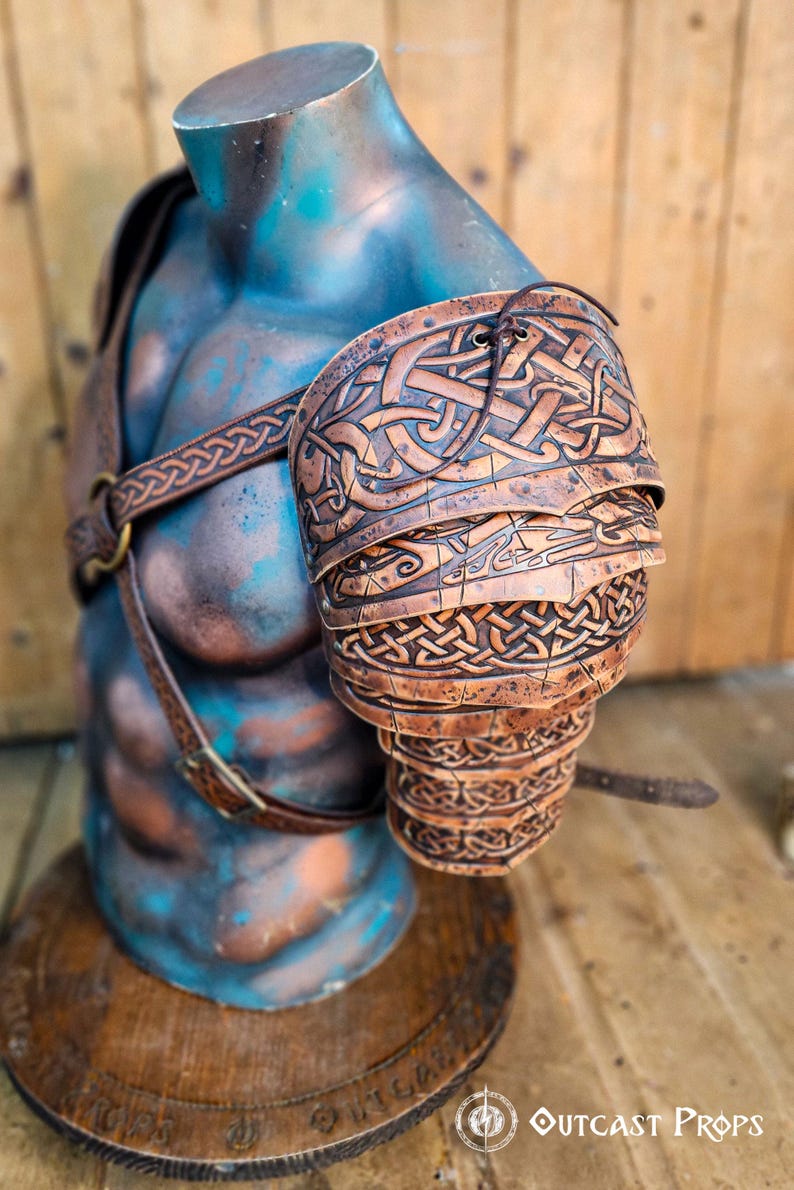Detailed side view of Sedrik Viking leather shoulder armor, showing layered brown leather plates engraved with Celtic knotwork and aged patina. Armor worn on a sculpted mannequin torso with embossed leather straps crossing the chest. Rustic wooden backdrop complements the handcrafted finish. Perfect for Viking warrior cosplay, Celtic LARP armor, Norse costume gear, fantasy medieval reenactment outfit, premium leather shoulder pauldrons.