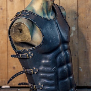 Side view of black leather Roman musculata cuirass with antique brass buckles and reinforced rivets, designed for LARP, Roman cosplay, or fantasy warriors. The sculpted abs and historical fit evoke the classical Greek ideal. Leather textures and shaped contours make the armor accessible to visually impaired users by enhancing tactile detail. Handmade and dyed with eco-friendly methods.