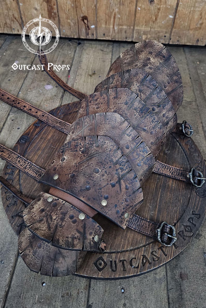 May include: A handcrafted, weathered-look leather and wood shield with riveted accents and buckle straps. The shield features the text "OUTCAST PROPS" and is designed for cosplay or display.