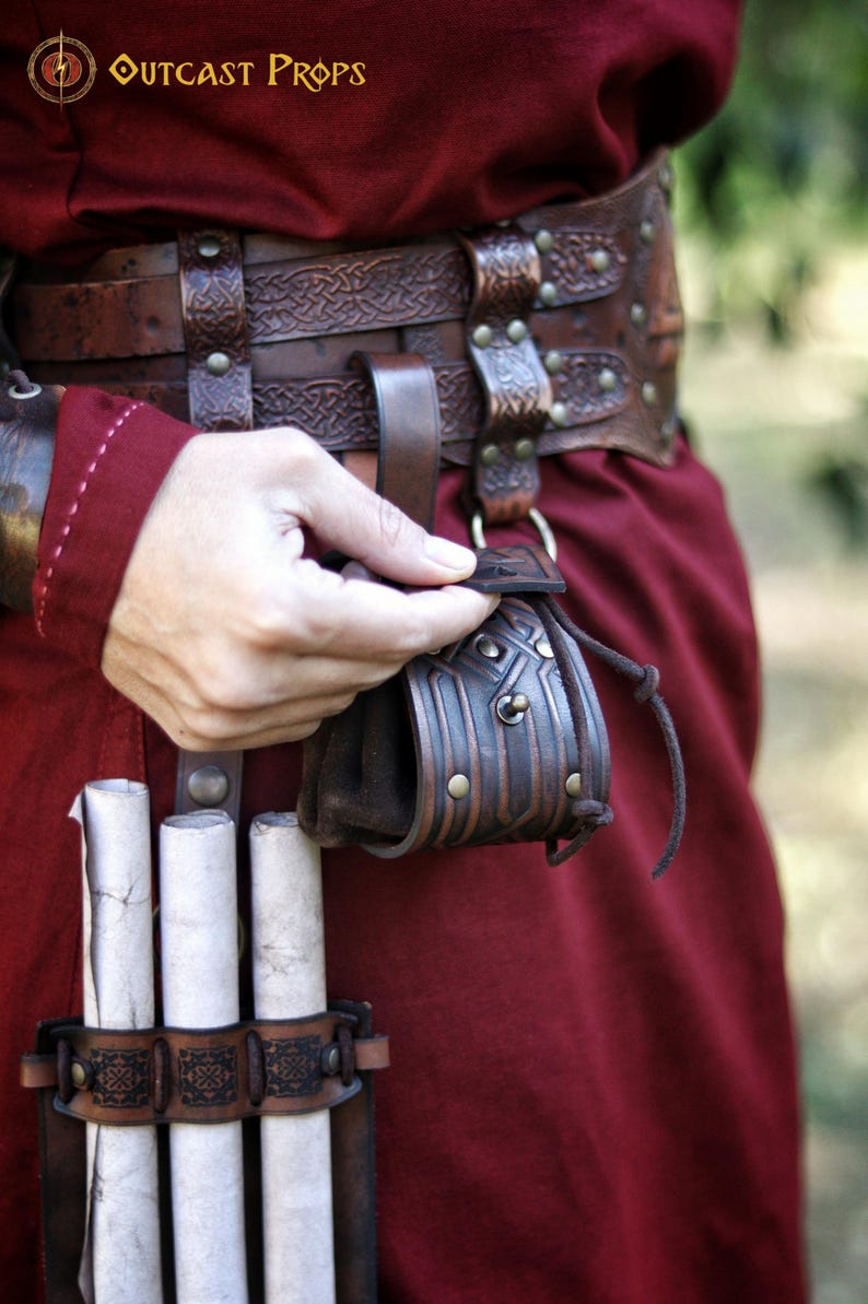 Detail view of a handcrafted leather coin pouch attached to a wide leather belt. Embossed geometric patterns inspired by Celtic and Viking motifs, aged brown leather finish, and drawstring closure. Compact pouch designed for coins, dice, keys, or small personal items. Ideal for fantasy characters, dwarven or medieval costumes, LARP, Renaissance fairs, or everyday leather accessories with character. Leather coin pouch with Celtic or Viking embossing,