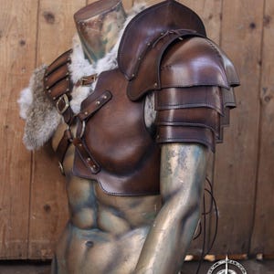 Frontal angle showing the structured design of the leather chest harness and right shoulder pauldron. Triple-layer leather plates form the pauldron, stitched and riveted by hand. The adjustable harness wraps around the torso for comfort and fit. Rich aged brown tones and texture reflect its post-apocalyptic, Viking, or fantasy warrior aesthetic. Designed for cosplay and immersive LARP combat.