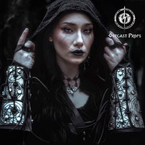 Sorceress in black cloak wearing pair of silver engraved bracers with magical protection symbols. Perfect for cosplay witches, warlocks, or demon hunter characters. These leather vambraces are handcrafted with riveted construction, elastic finger loops, and aged finish for a legendary look. Designed for gothic LARP, fantasy conventions or dark rituals. Demon Hunter Leather Bracers Armor for LARP Cosplay Witch Warlock Alchemist Magic Rune Occult Ritual Fantasy Medieval Costume Accessories