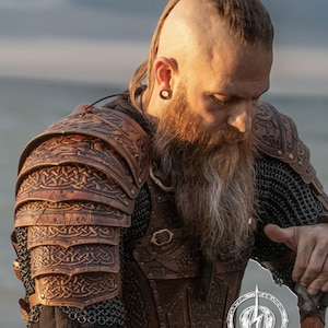Side profile of a mohawk-bearded LARP fighter wearing Sedrik viking leather shoulder armor with engraved Celtic knots, photographed at golden hour. The layered accordion-style pauldrons provide flexibility and cinematic aesthetics. Perfect for viking cosplay shoulder armor, Nordic LARP leather pauldrons, celtic warrior costume or medieval fantasy shoulder armor for immersive events and photoshoots.