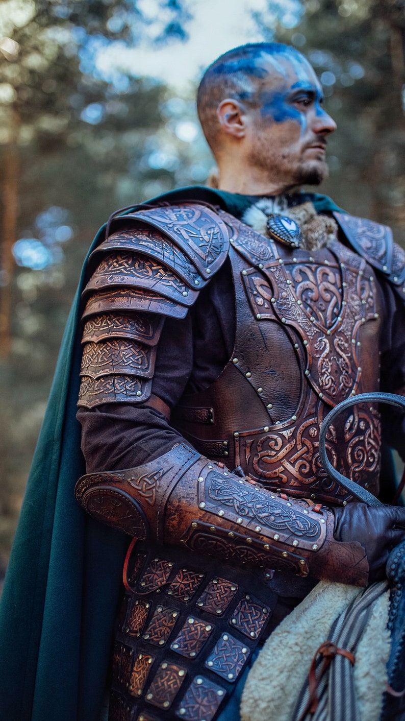 May include: A person wearing a leather armor with intricate carvings and a blue face paint. The armor is made of brown leather and has a Celtic knot design. The person is wearing a green cloak and is holding a sword.
