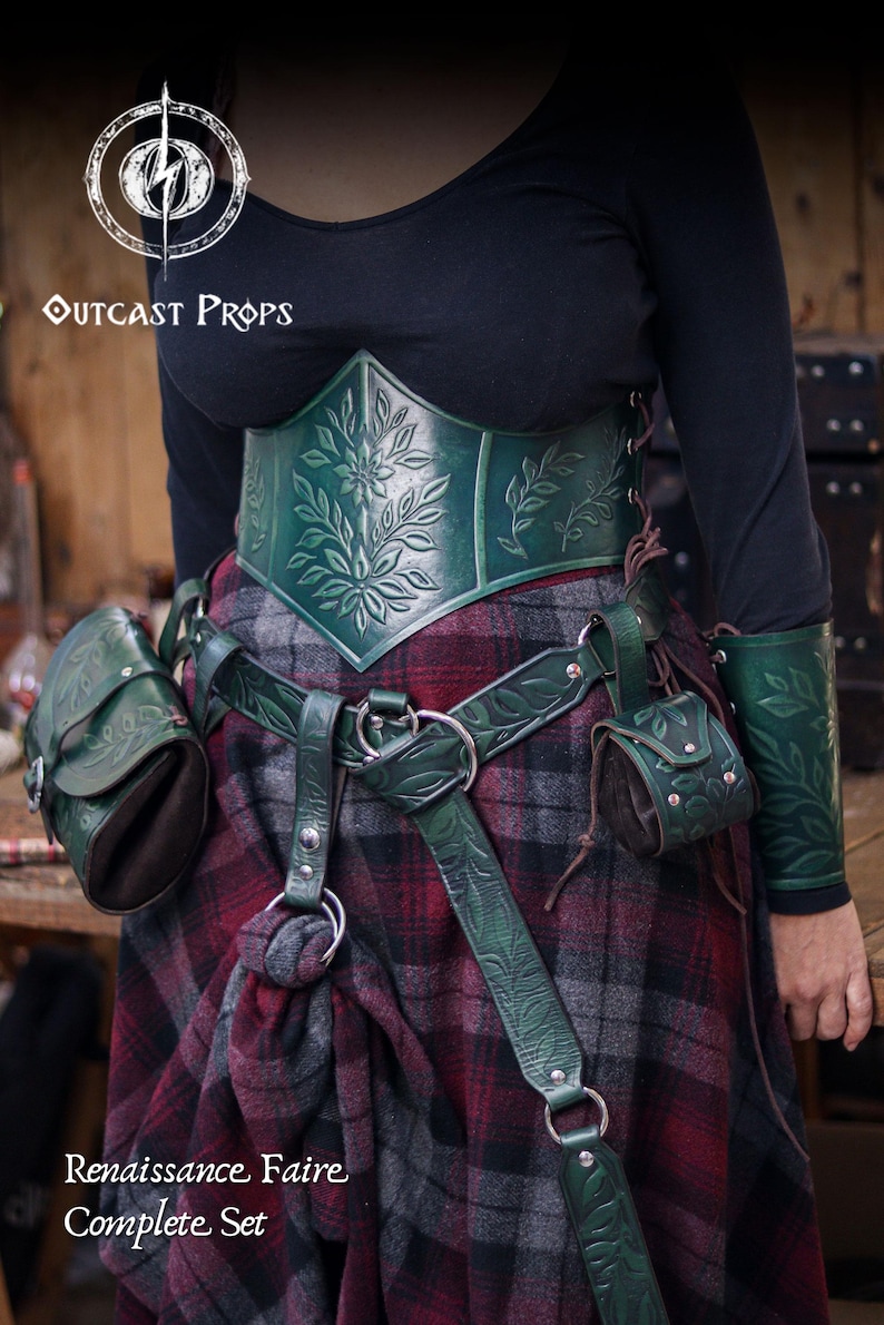 A model wears a full green leather set with embossed floral patterns, including corset, belt, hipbag and coin pouch. The pieces have botanical carvings and soft suede bodies, creating an elegant elven or herbalist look. The plaid skirt enhances the renaissance faire style. This fantasy outfit shows how the floral coin pouch attaches to the belt, making it suitable for witches, nobles and renfaire characters who need a practical accessory for coins or dice.