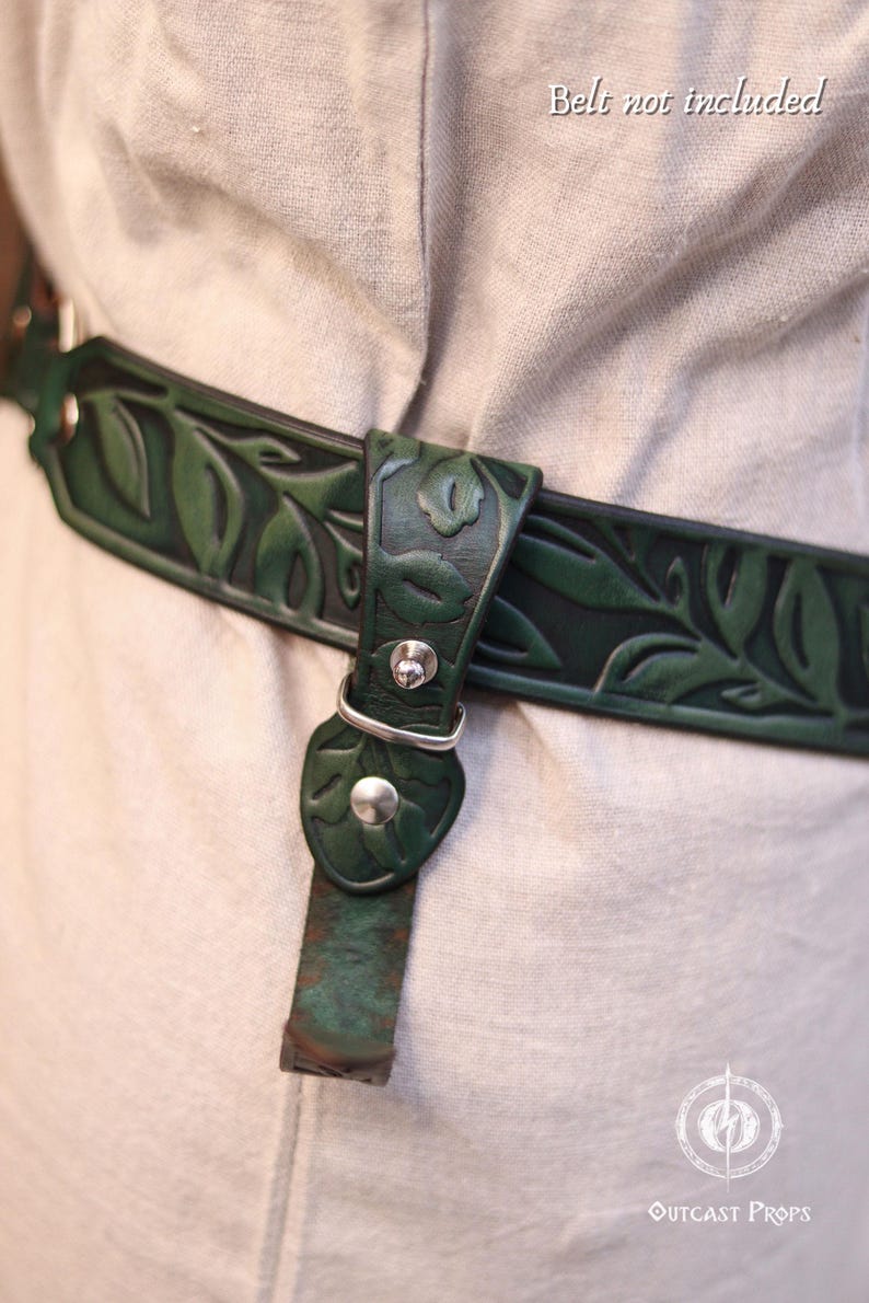 May include: A dark green leather belt with a leaf pattern, secured with a silver buckle. The belt is worn over a light-colored garment. The text "Belt not included" is visible. The Outcast Props logo is in the bottom right corner.