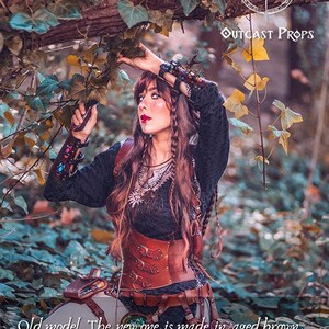Female adventurer in the forest wearing the old brown leather corset model. The new edition is crafted in aged brown with nickel hardware and more elegant buckles. Designed for witches, alchemists, and fantasy LARP characters, this steampunk waist cincher combines historical style and eco-tanned leather craftsmanship, ideal for renaissance fairs, gothic events, and fantasy festivals.