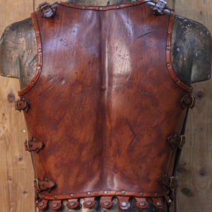 Close-up leather Roman gladiator armor, displaying detailed muscle shaping and battle scratches. This musculata cuirass is ideal for LARP events, cosplay warriors, and reenactment fans. Made with vegetable-tanned leather and hand-riveted accents, it mimics the heroic physique of Roman generals and fantasy heroes with striking realism.