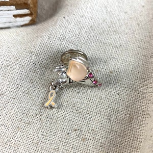 May include: Silver tone pin with a pink stone and a pink ribbon charm. The pin is in the shape of a heart with pink rhinestones around the edge.